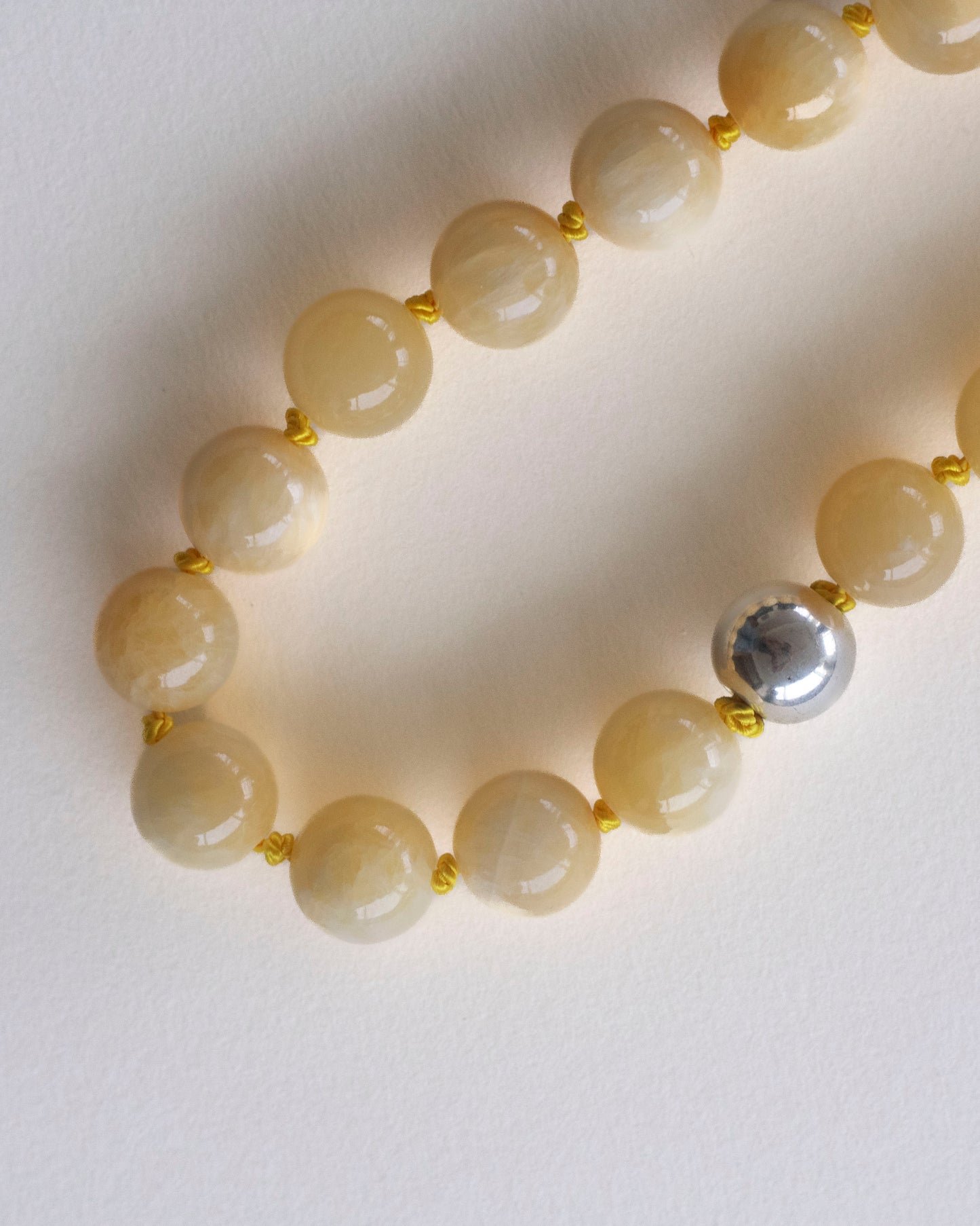 detail of Necklace crafted in honey jade beads hand-knotted on yellow silk thread, with one single 925 sterling silver bead,