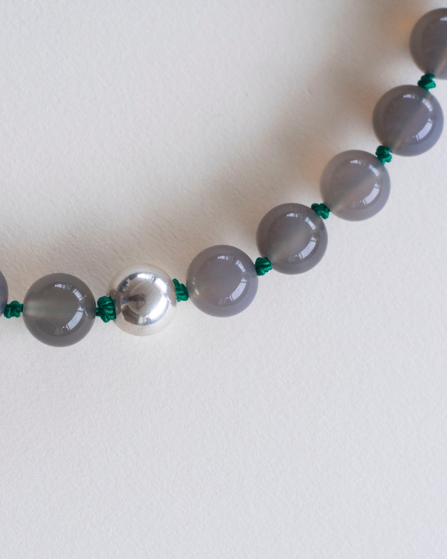 Gray agate beaded necklace with silver clasp on a white background and handknotted on emerald green silk thread