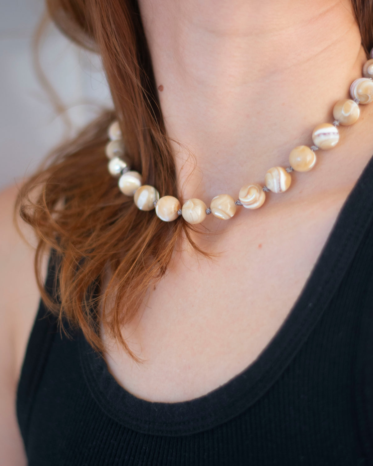 mother of Pearl hand-knotted necklace on grey silk being worn on a person's neck with a blurred background