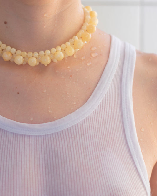 Close-up of a model wearing a honey jade, handmade beaded necklace and a white tank top.