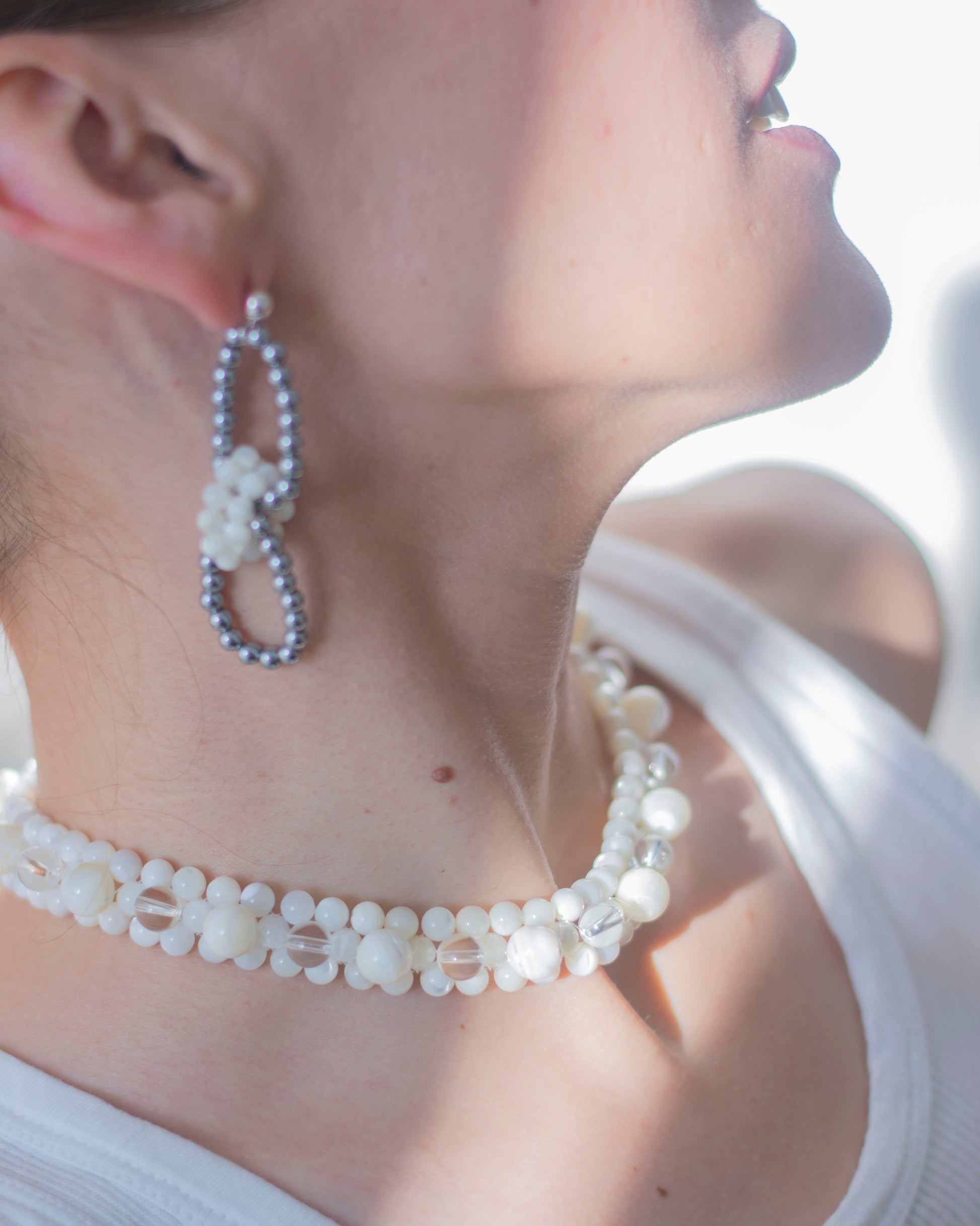 Close-up of a person wearing pearl and hematite earrings and necklace with blurred background