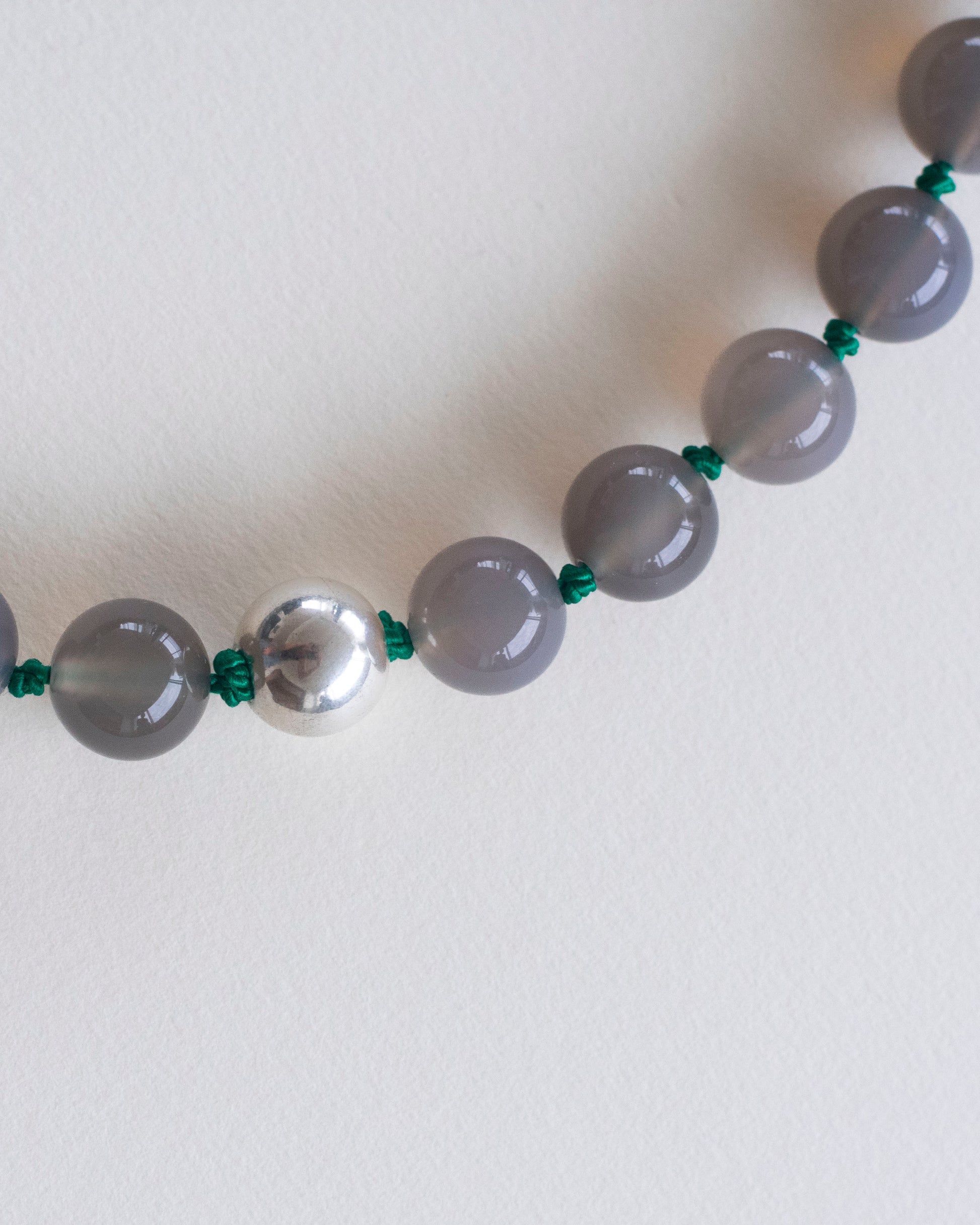 Gray agate beaded necklace with silver clasp on a white background and handknotted on emerald green silk thread