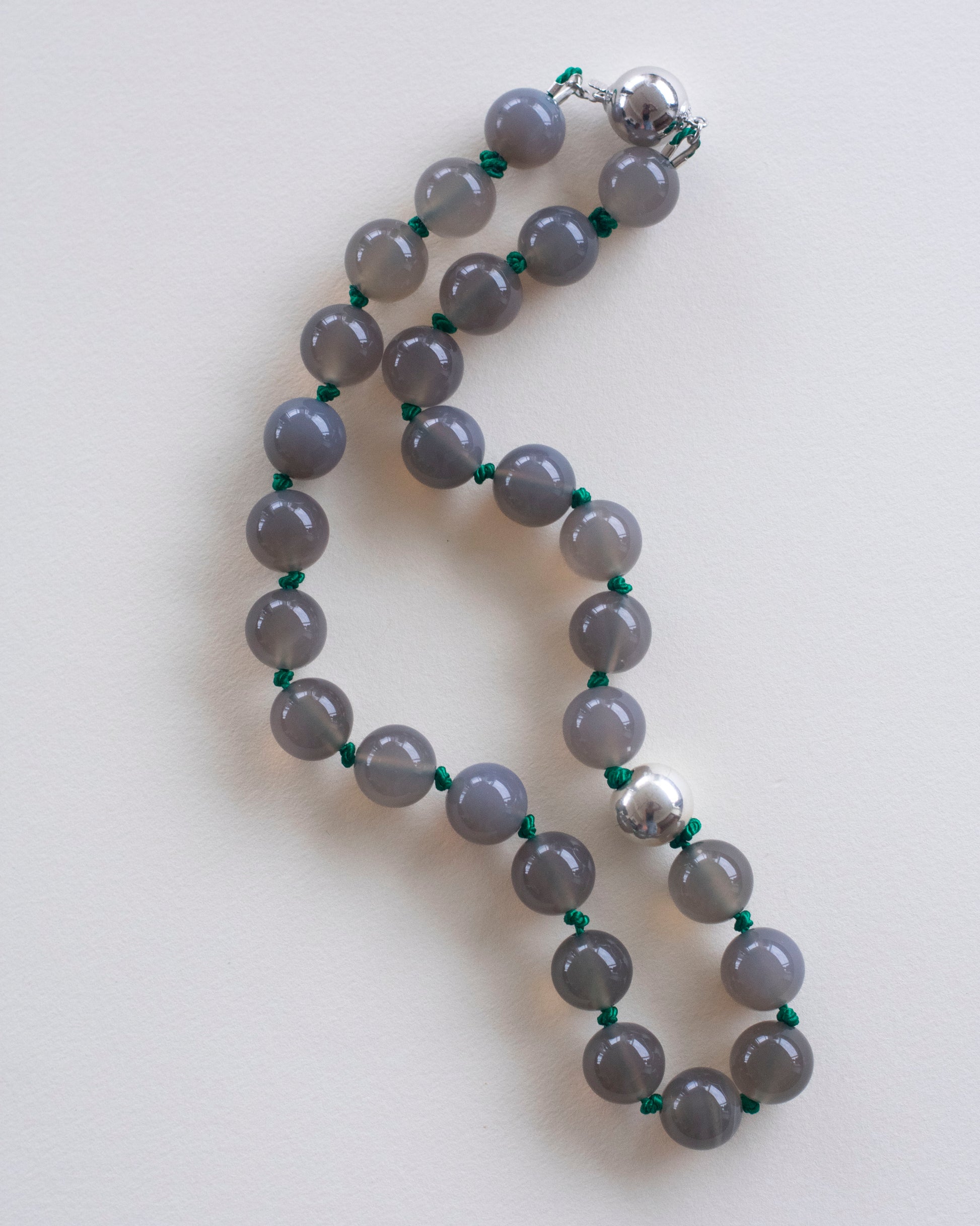 Gray agate beaded necklace with silver clasp on a white background and handknotted on emerald green silk thread