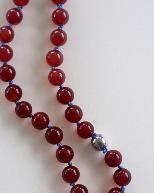 Beaded necklace with red carnelian beads , hand-knotted on light blue silk thread and festuring a 925 sterling silver bead and clasp on a light pink background
