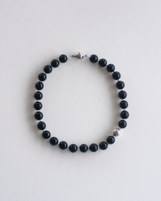 Black onyx beaded necklace, hand-knotted on off-white silk thread and featuring one 925 sterling silver bead, laid flat on a white background