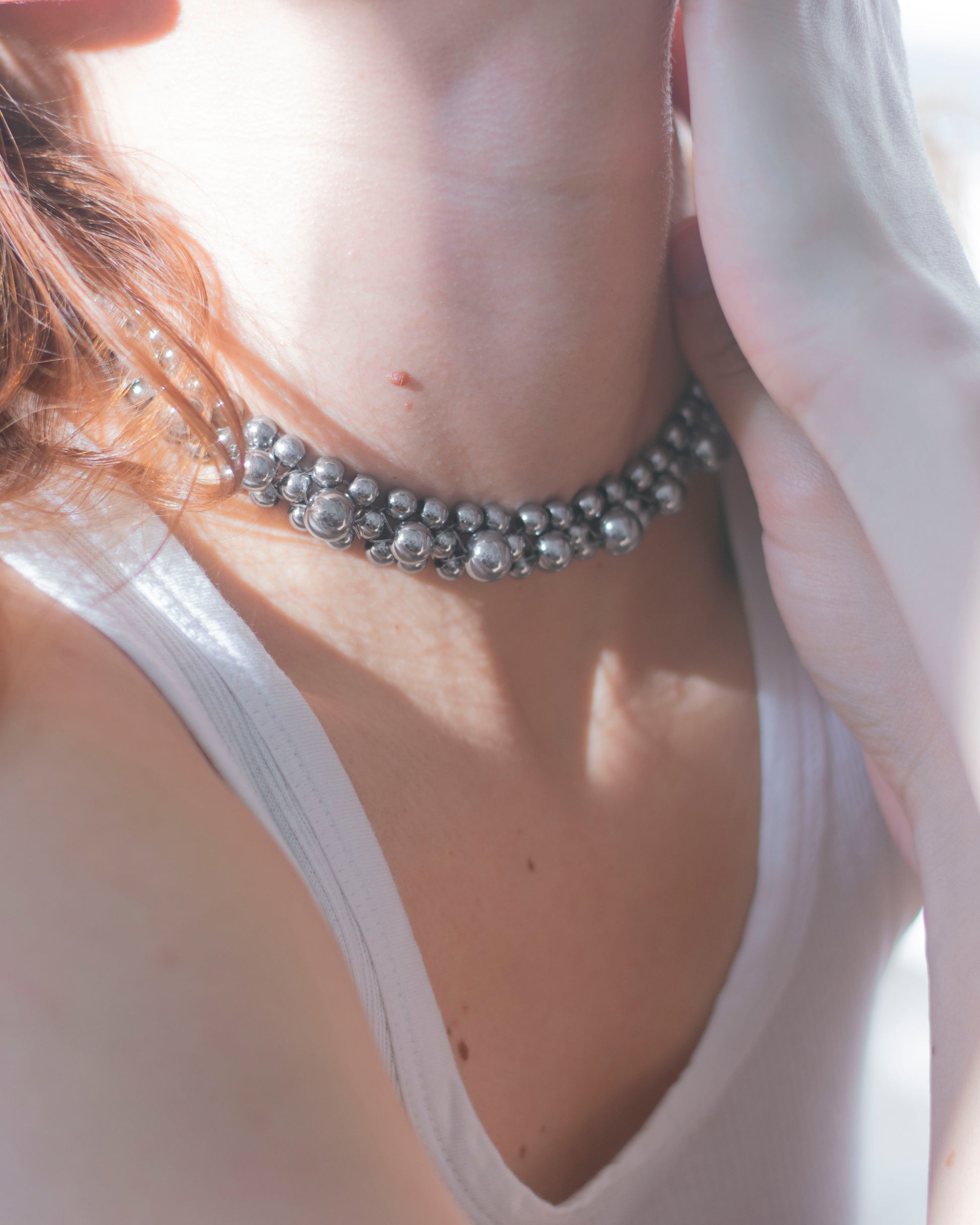 Close-up of a person wearing a silver hematite double-layered beaded necklace with a blurred background