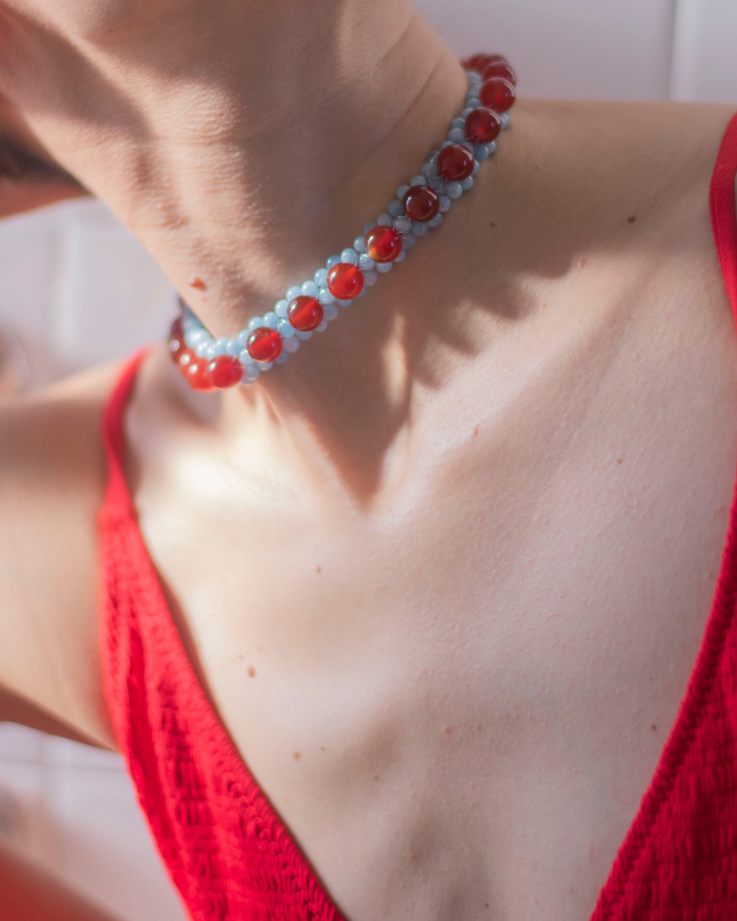 Close-up of a person wearing a red  carnelian and aquamarine beaded necklace with a red top.