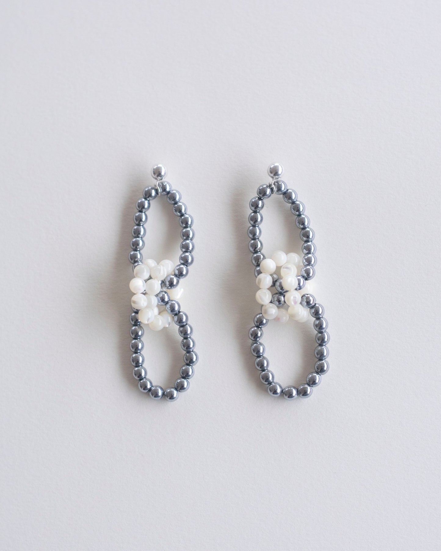 Pair of beaded earrings in hematite and mother of pearl on a light gray background