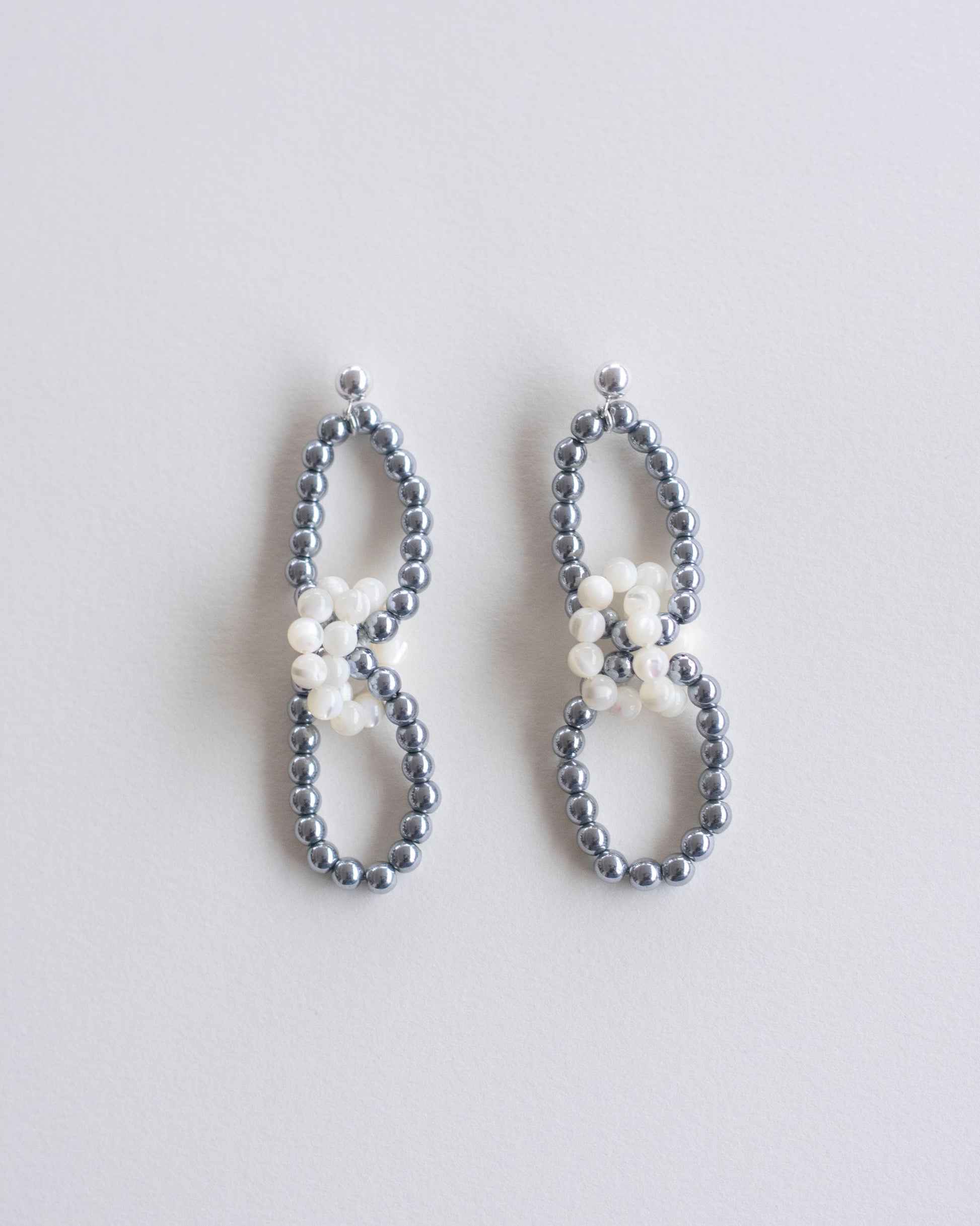 Pair of beaded earrings in hematite and mother of pearl on a light gray background