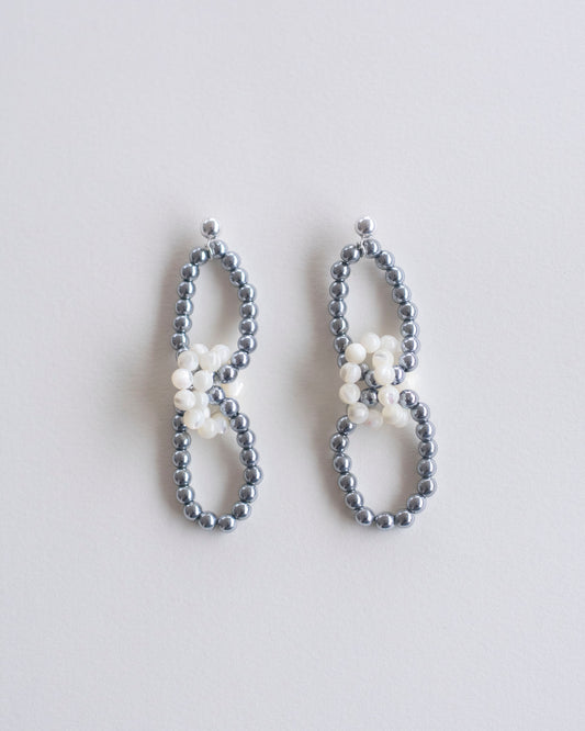 Pair of beaded earrings in hematite and mother of pearl on a light gray background