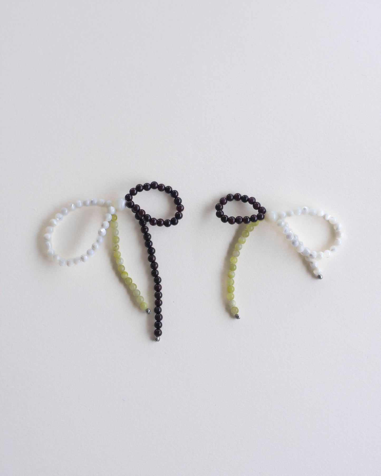 a pair of earrings made in mother of pearl, garnet and lemon jasper, featuring a bow form, laid flat on a white background.