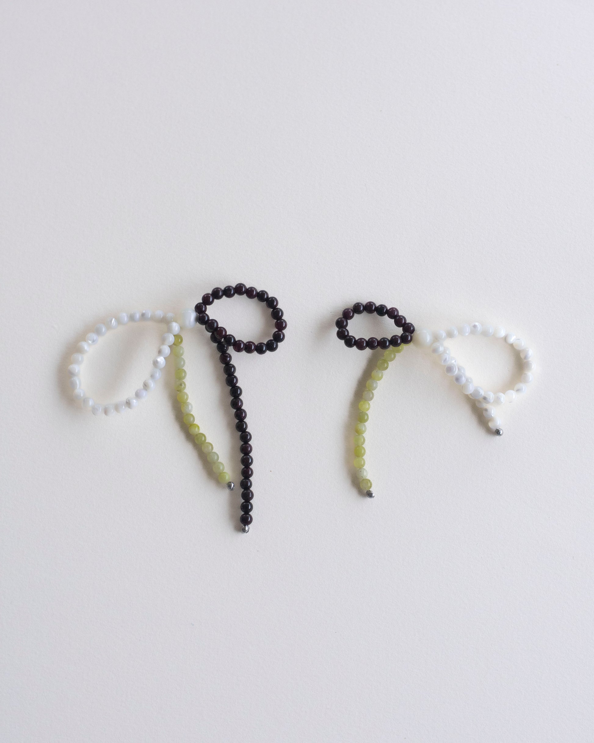 a pair of earrings made in mother of pearl, garnet and lemon jasper, featuring a bow form, laid flat on a white background.