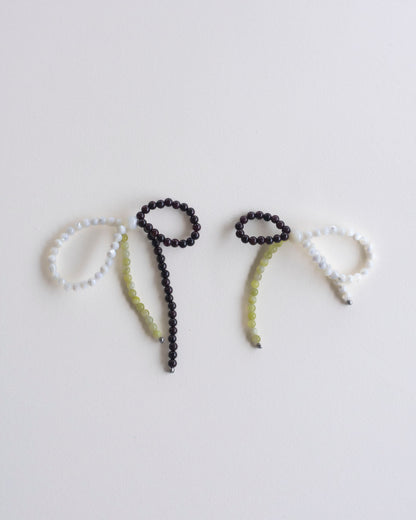 a pair of earrings made in mother of pearl, garnet and lemon jasper, featuring a bow form, laid flat on a white background.