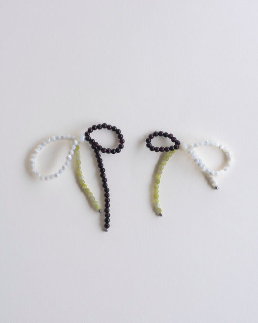 a pair of earrings made in mother of pearl, garnet and lemon jasper, featuring a bow form, laid flat on a white background.