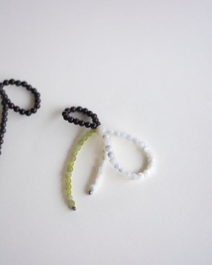detail of an earring made in mother of pearl, garnet and lemon jasper, featuring a bow form.