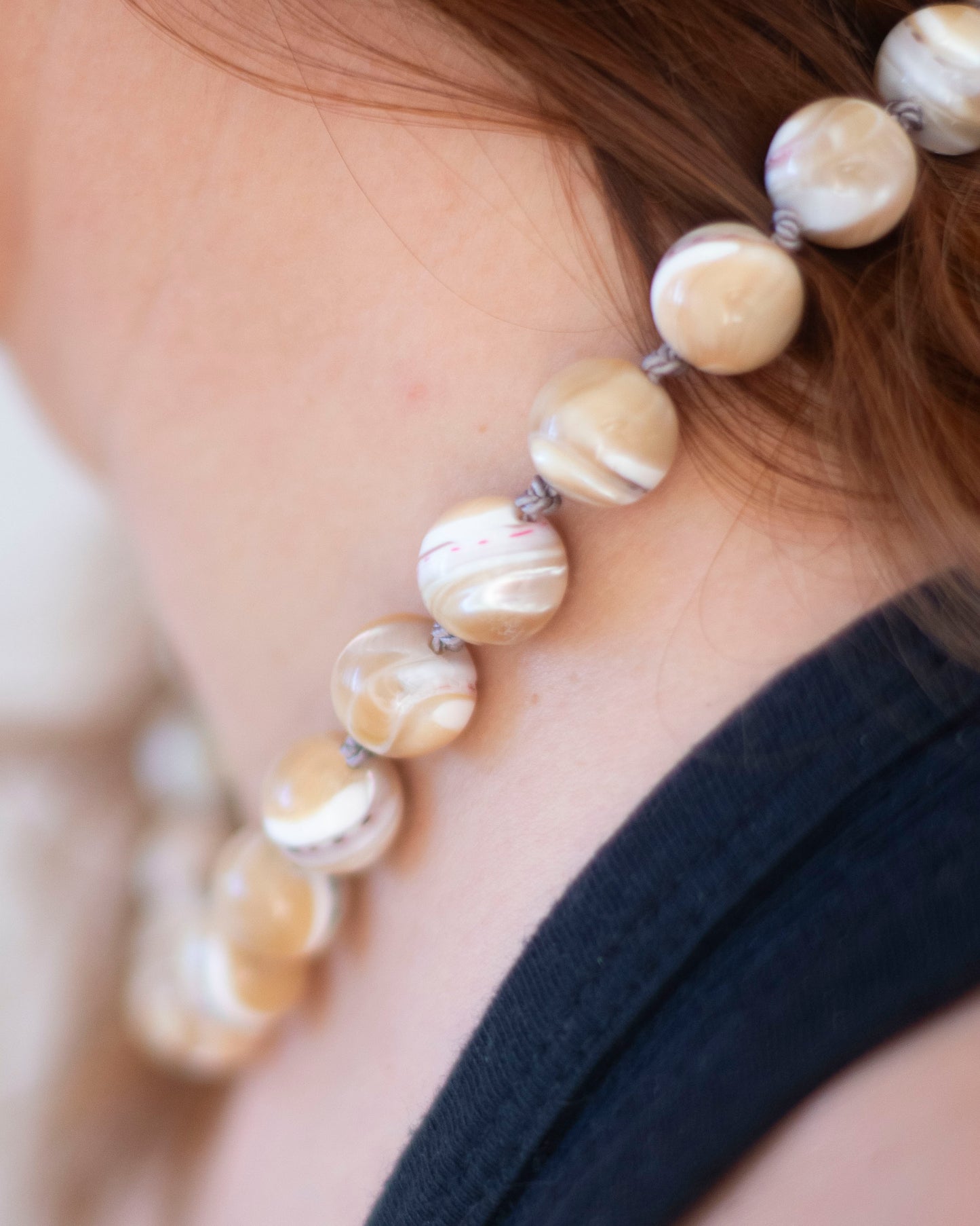 mother of Pearl hand-knotted necklace on grey silk being worn on a person's neck with a blurred background