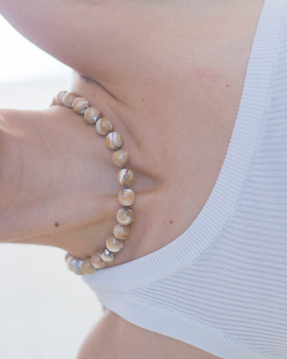 Necklace with beige MOTHER OF PEARL beads worn by a person against a white background