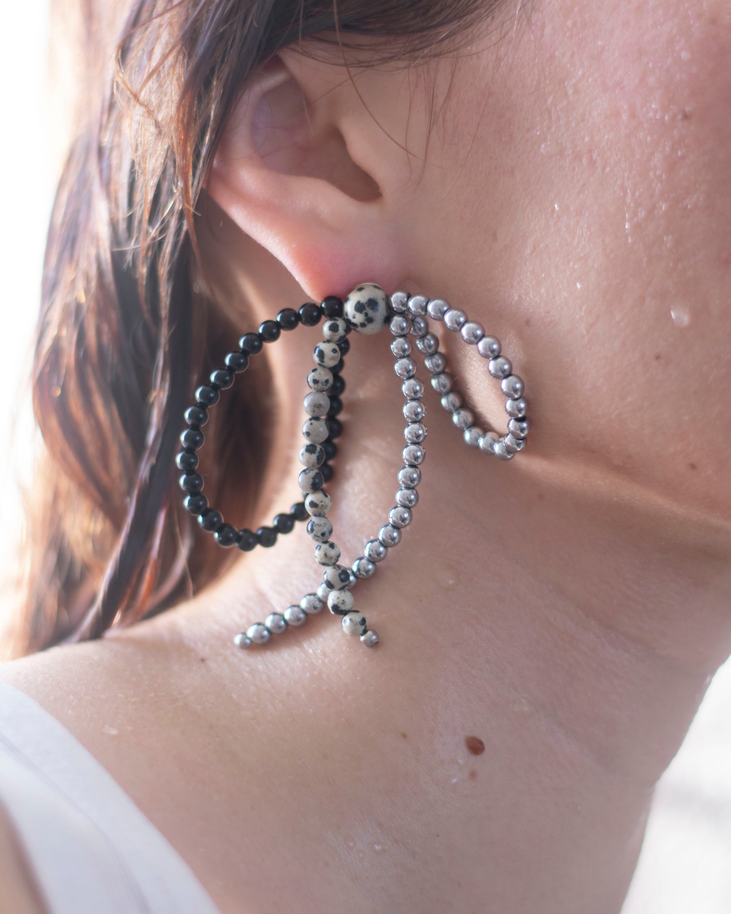Close-up of an ear wearing a black onyx, hematite and dalmatian jasper beaded earring with  a bow shape