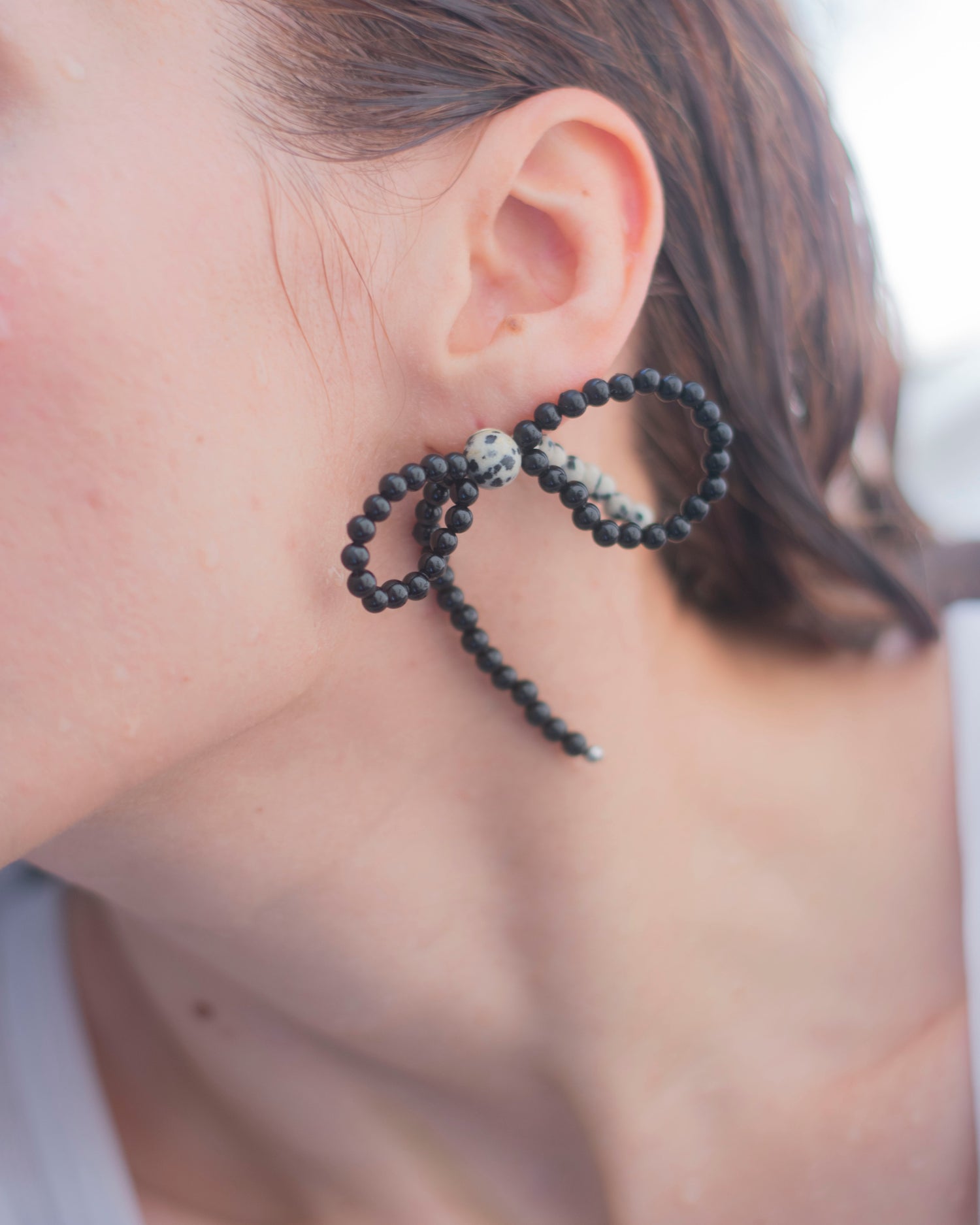 Close-up of an ear wearing a black onyx and dalmatian jasper beaded earring with  a bow shape