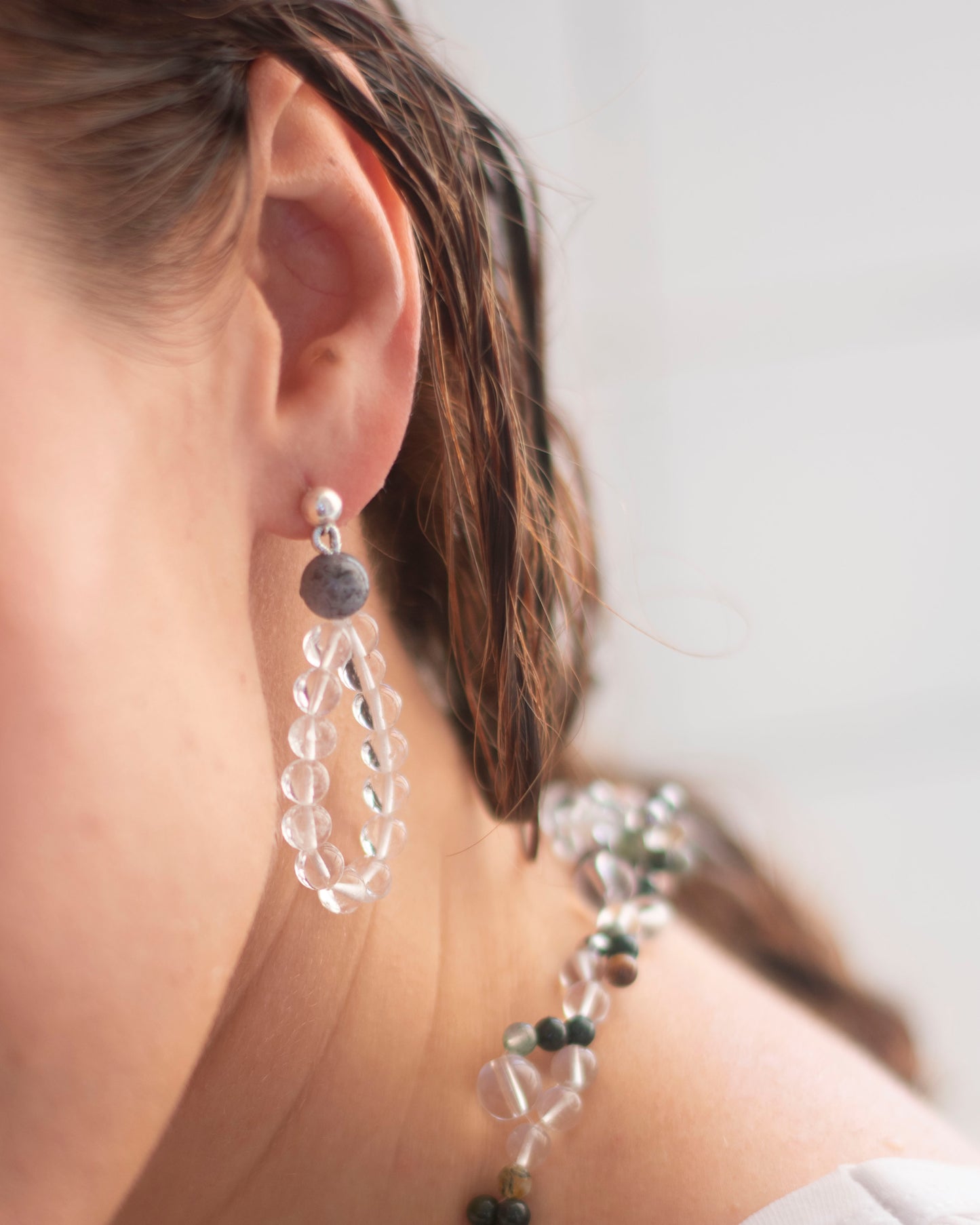 Close-up of a person wearing clear crystal quartz beaded earrings in a drop shape with a blurred background