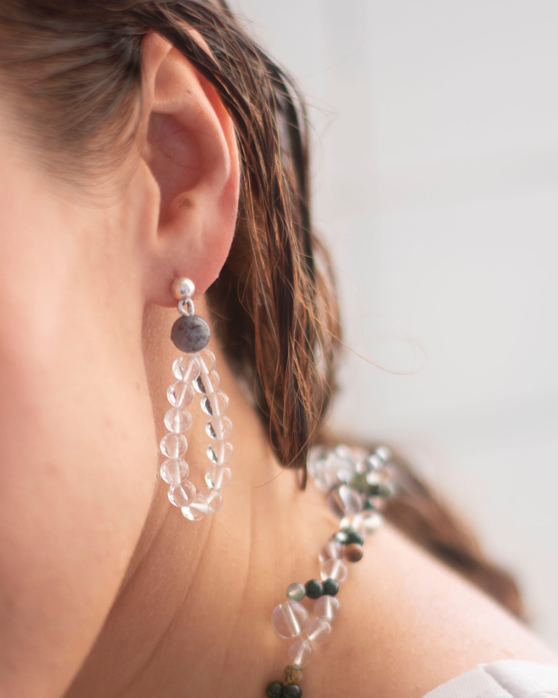 Close-up of a person wearing clear crystal quartz beaded earrings in a drop shape with a blurred background