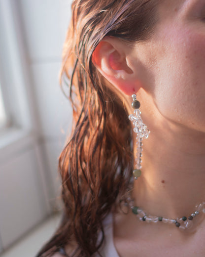 Close-up of a person wearing a beaded earring made in crystal quartz and indian agate with a blurred background