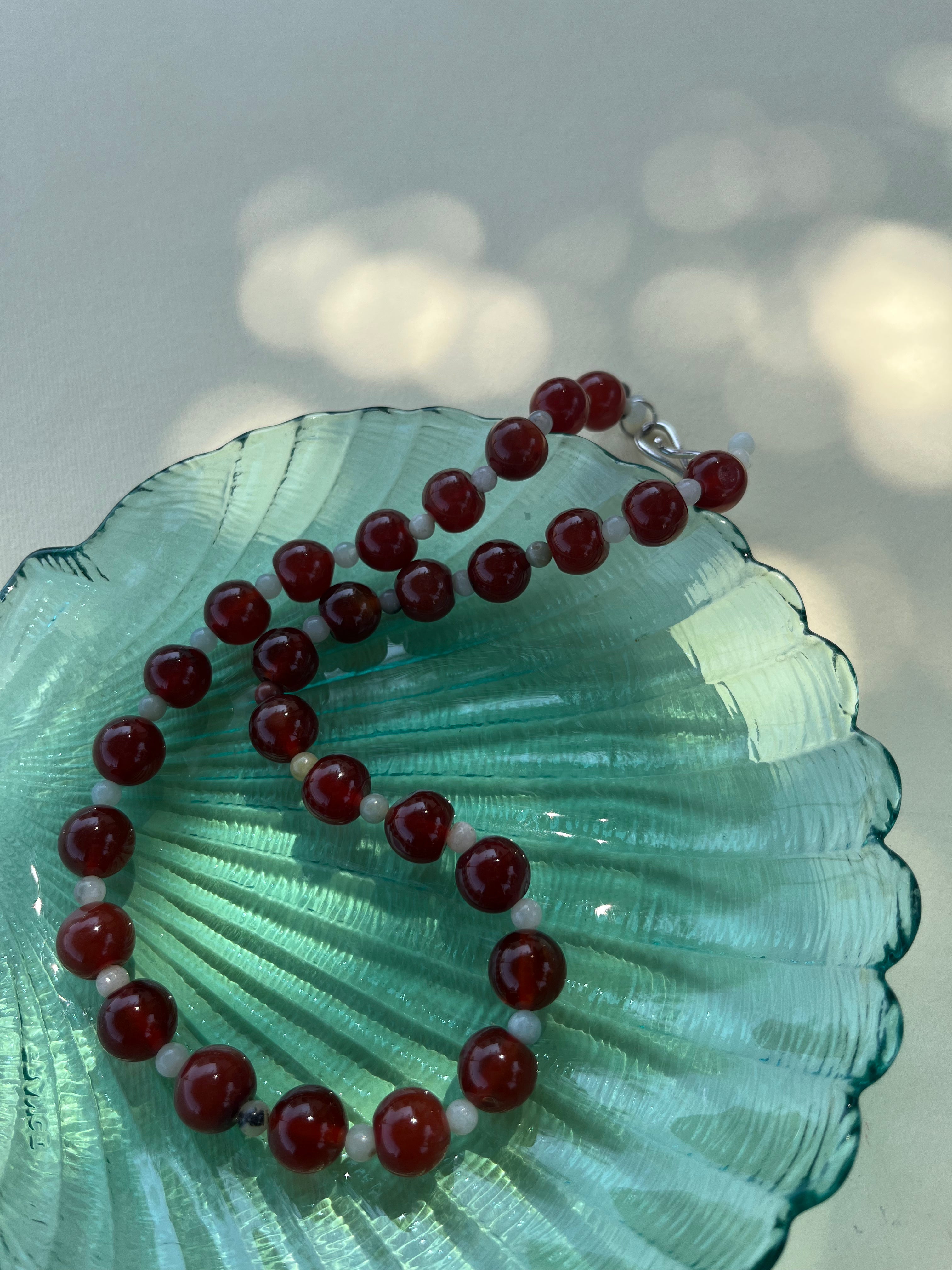 Red beaded bracelet on a green shell with a blurred light background. 