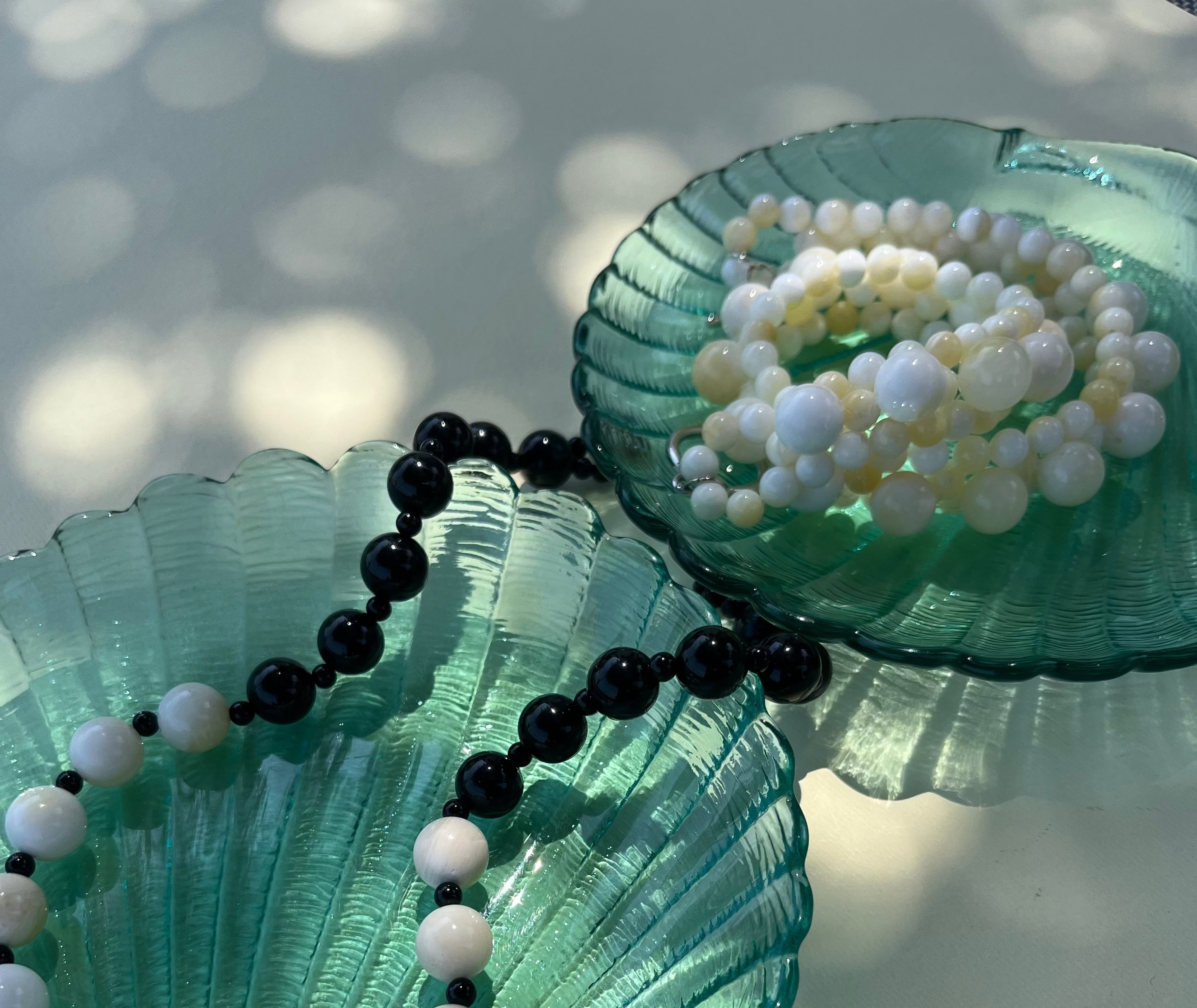 yellow shell and black obsidian beaded necklaces on green seashells with a blurred background. Ethically sourced, handmade and strung on silk thread.