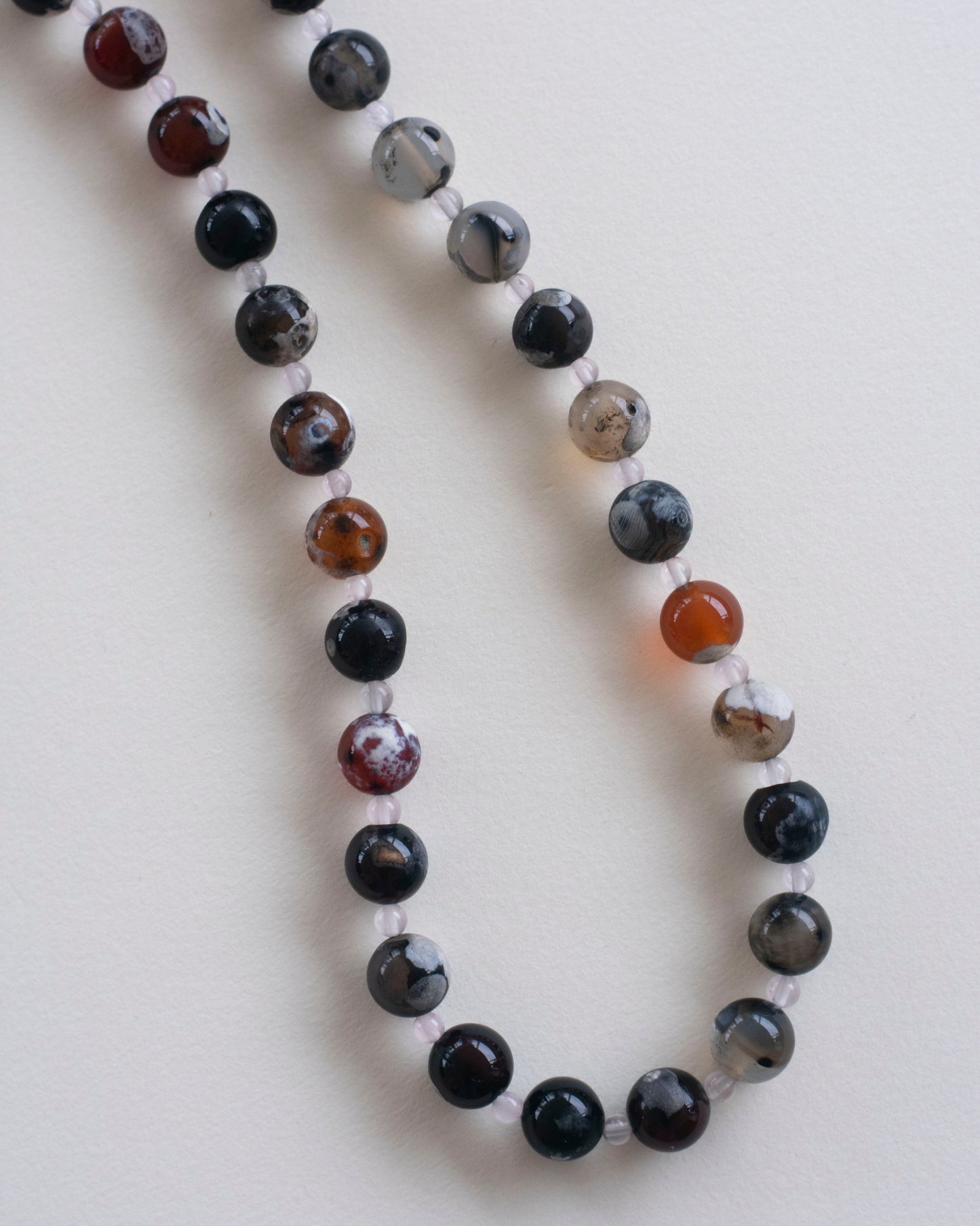 detail on fire lace agate and rose quartz beaded necklace on a light gray background