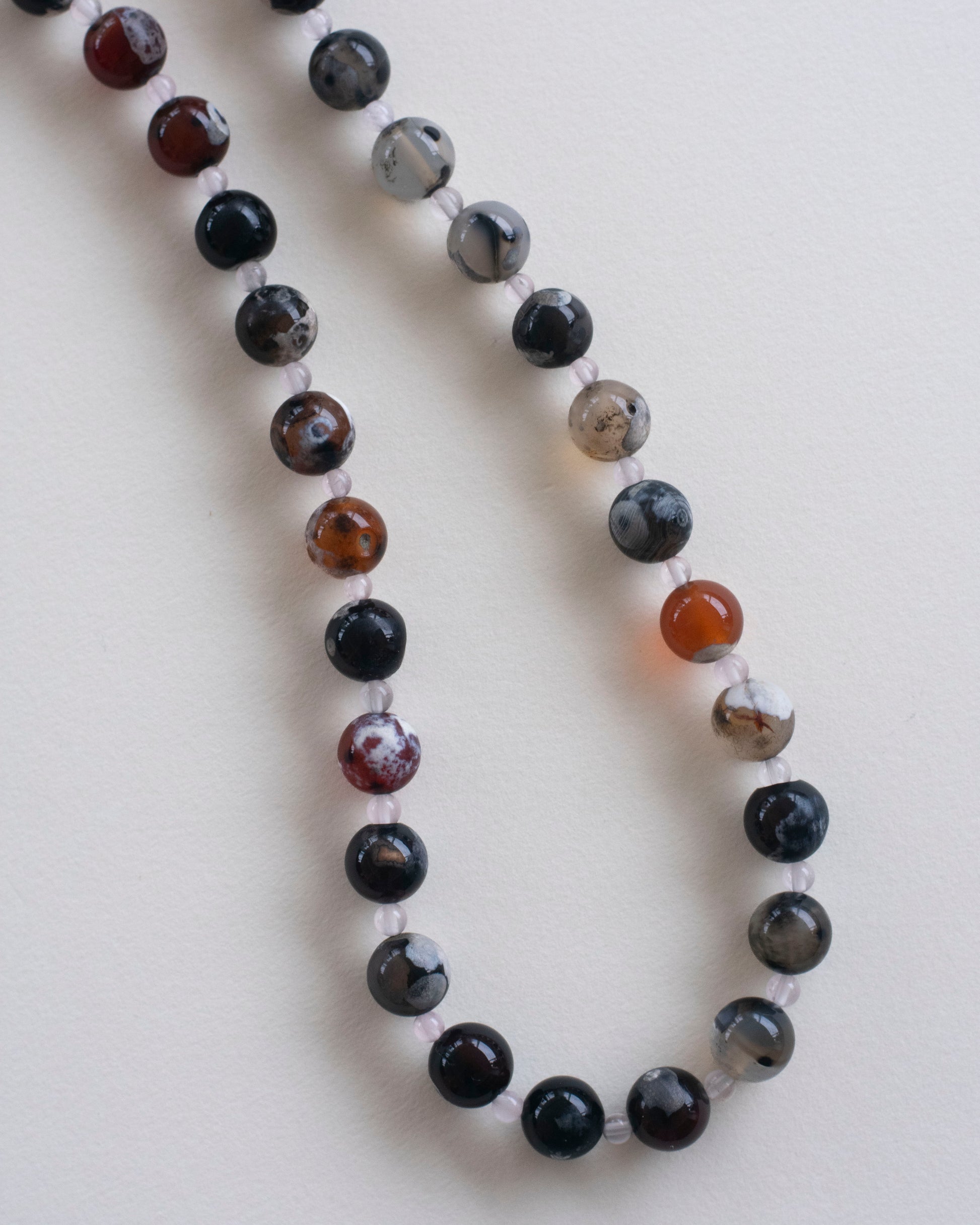 detail on fire lace agate and rose quartz beaded necklace on a light gray background