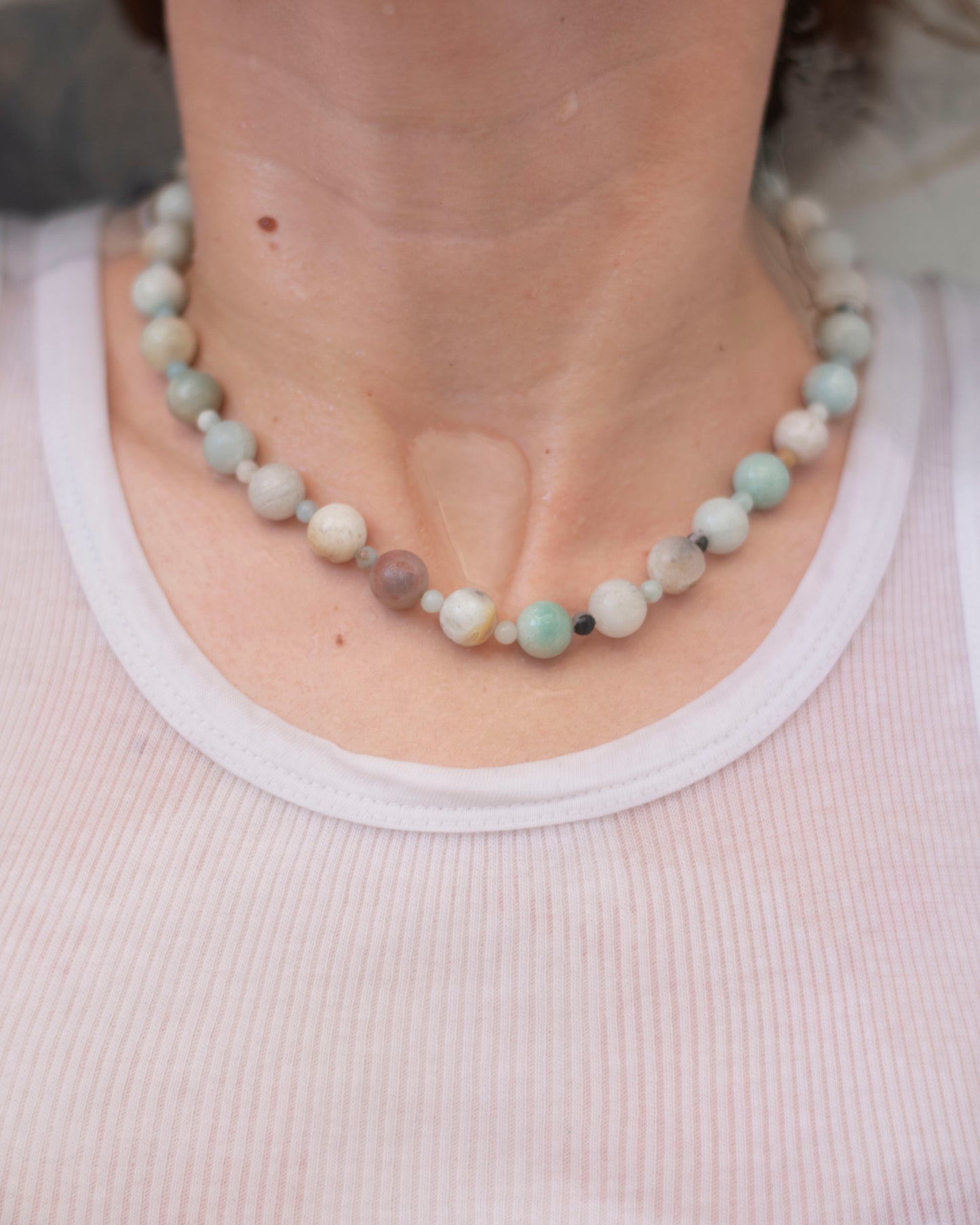 Close-up of a person wearing an amazonite beaded necklace with a plain background