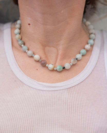 Close-up of a person wearing an amazonite beaded necklace with a plain background