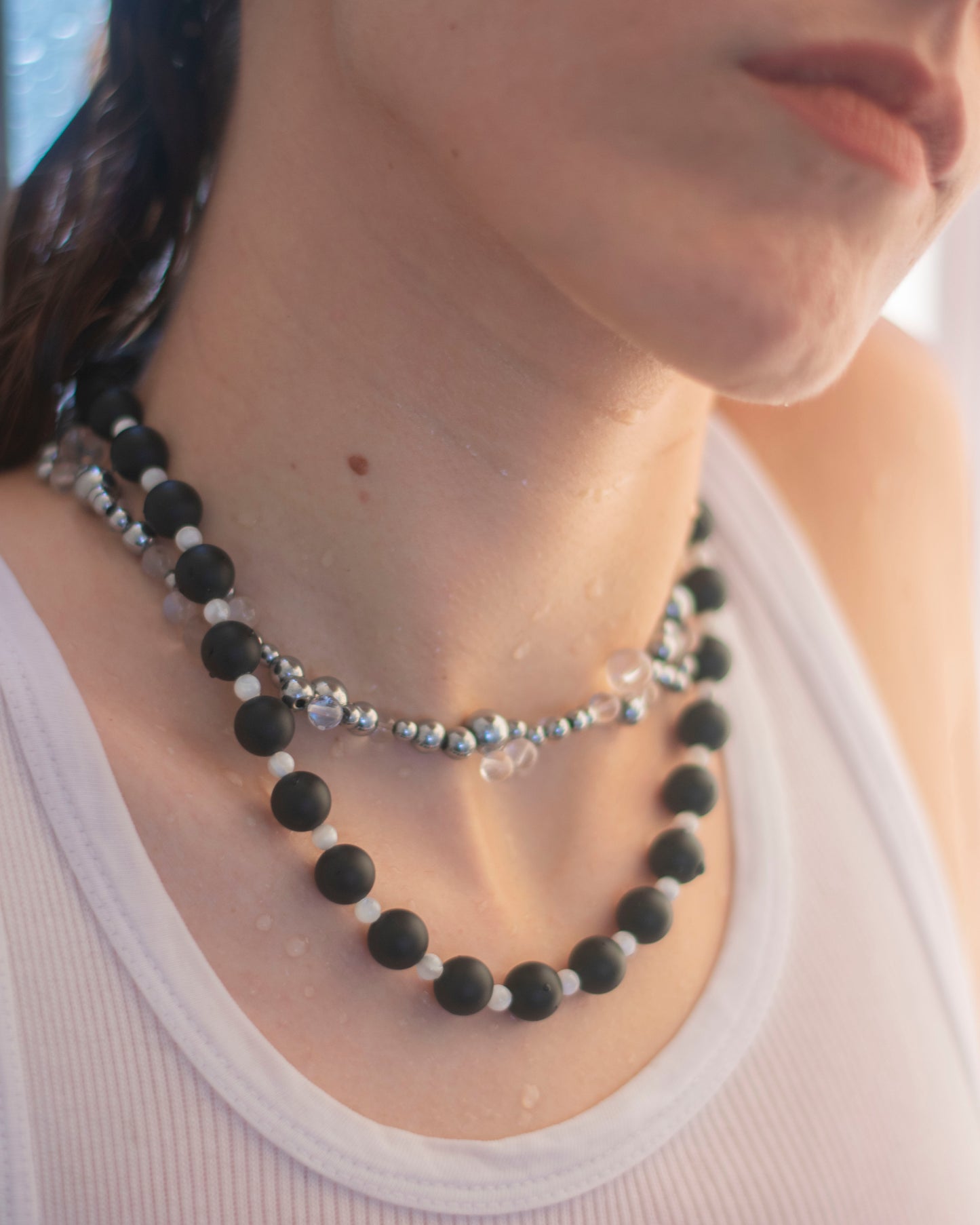 model wearing two beaded necklaces made in black matte agate and mother of pearl, on a white tank top.