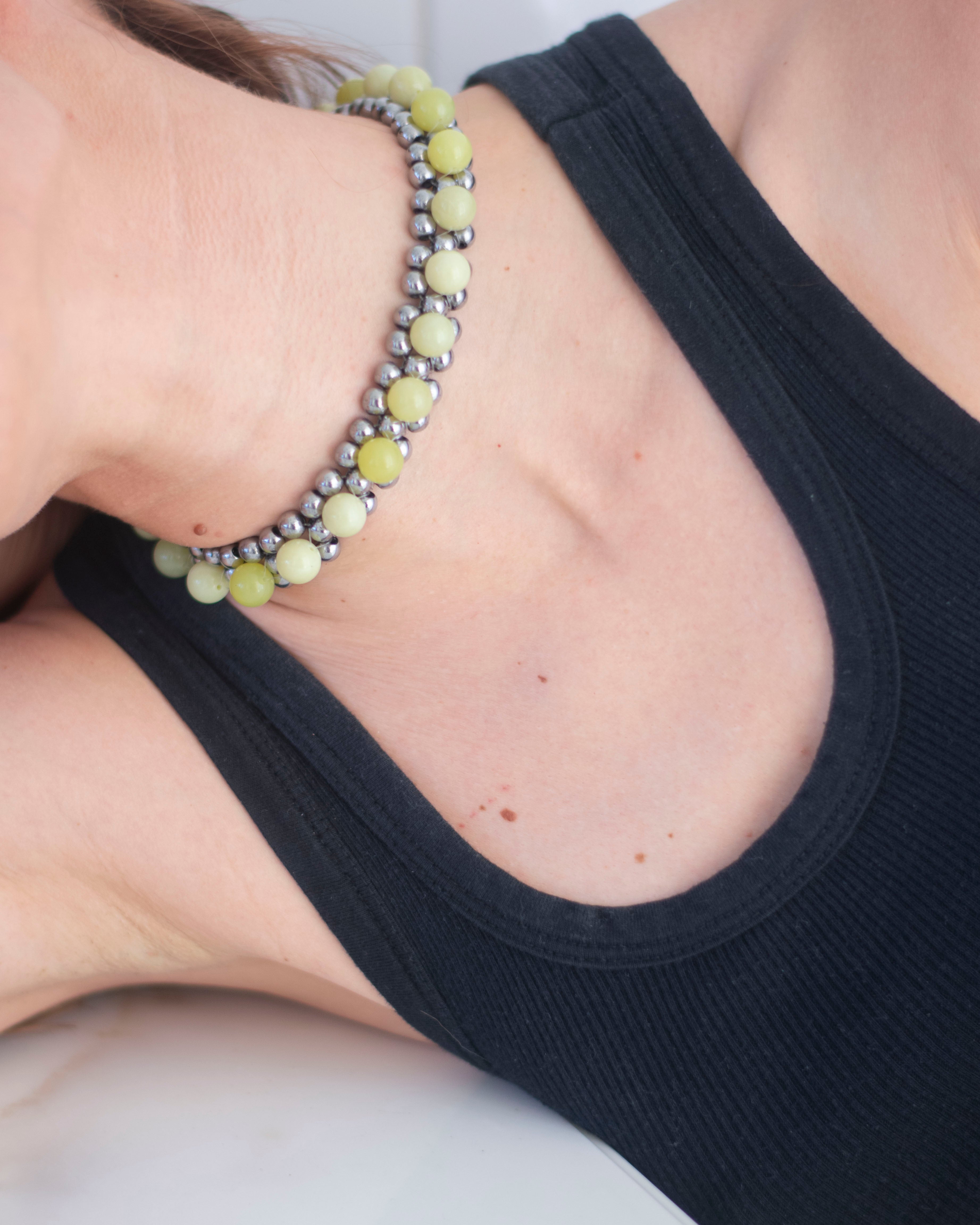 Close-up of a person wearing a black tank top with double layered beaded necklace, made with hematite and lemon jasper, on her necklace